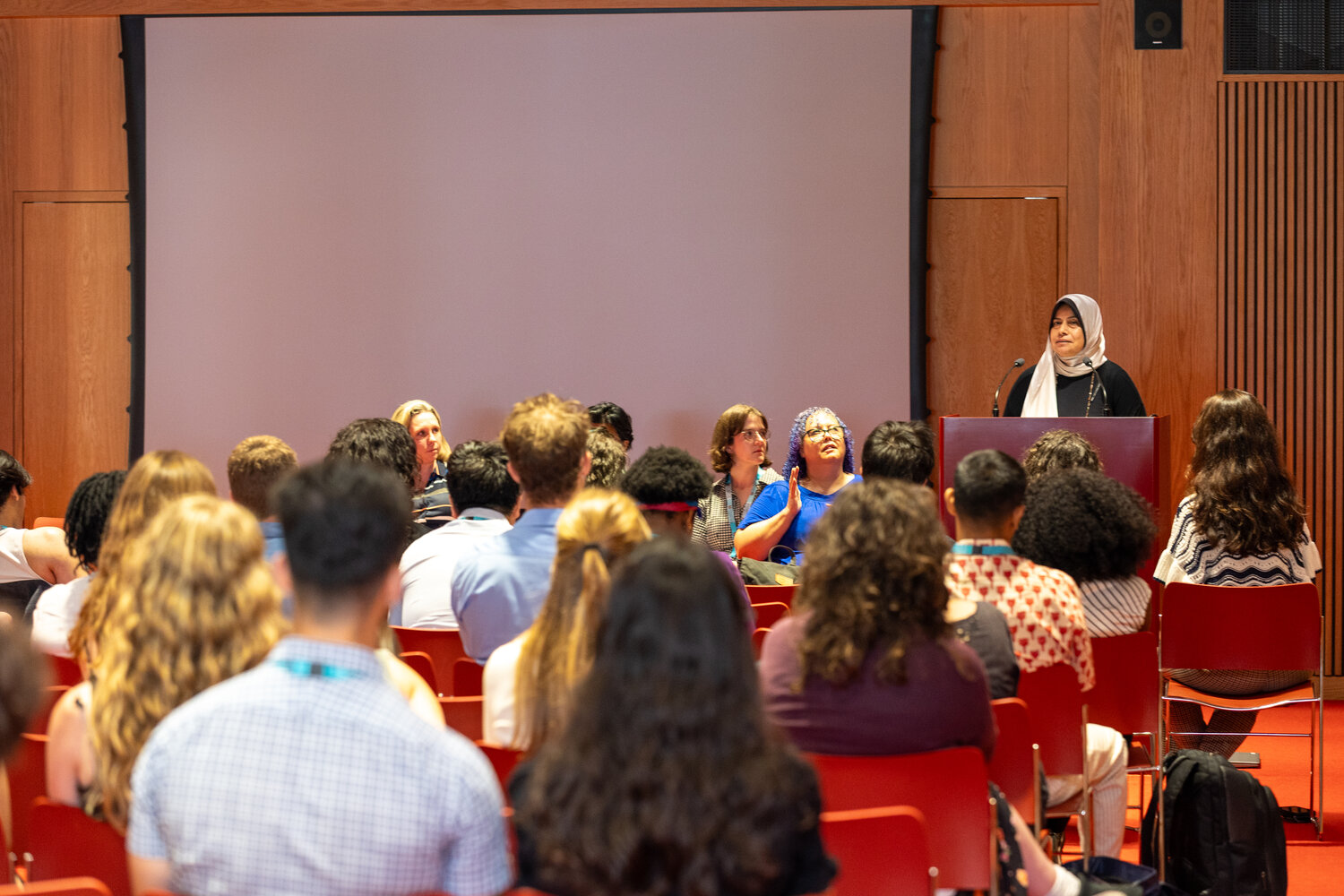 Woman in hijab at lecturn speaking to a group of people