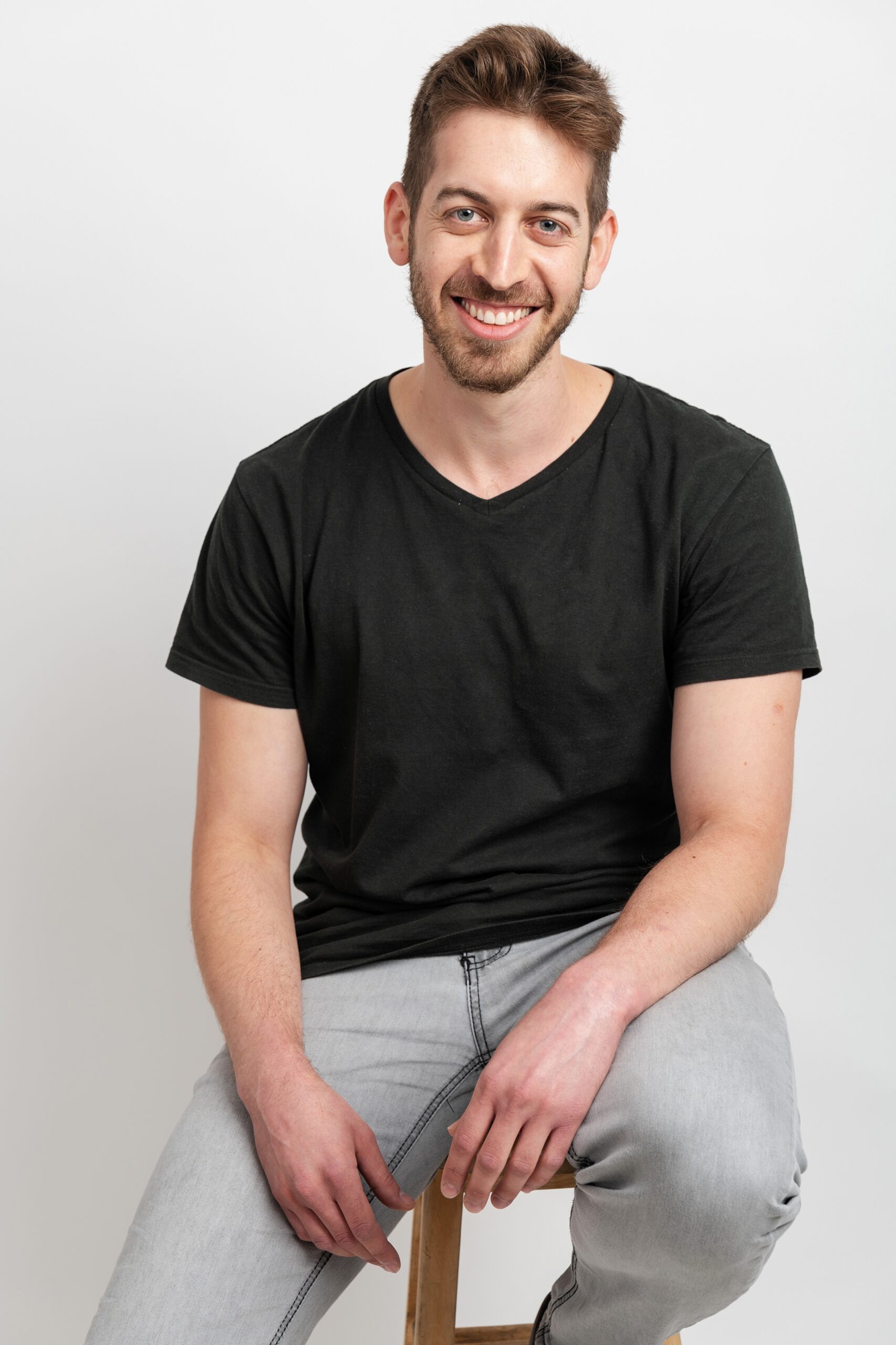 Man sitting on stool in t-shirt and jeans smiling